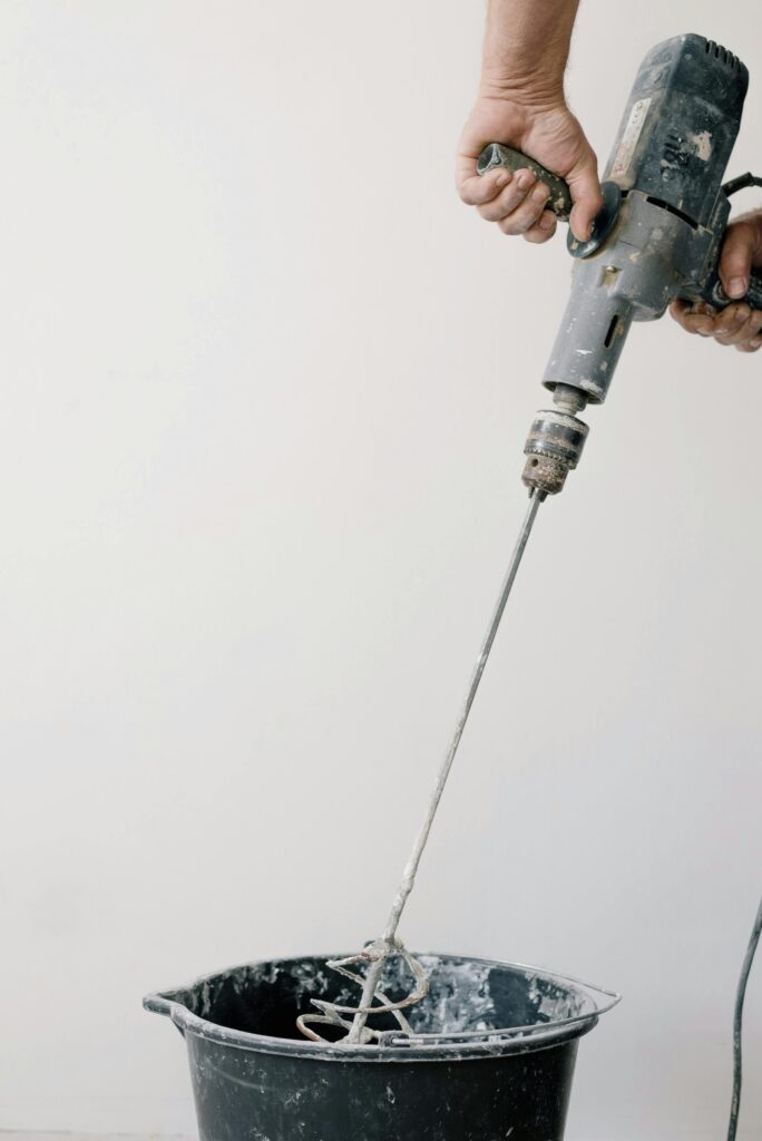 Crop unrecognizable male worker holding drill with tool and mixing cement in plastic container